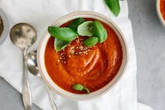 two bowls of roasted red pepper soup with basil garnish and spoons on the side