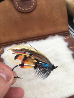 a person is holding a fly with feathers on it in front of a brown leather case