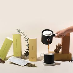 a person pours coffee into a cup from a black mug in front of several boxes