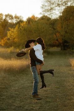 a man and woman kissing in the middle of an open field with trees in the background