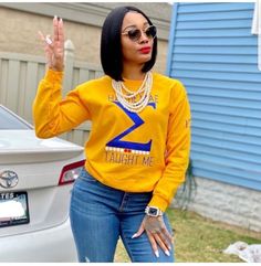 a woman standing next to a white car wearing a yellow shirt and blue jeans with her hands in the air