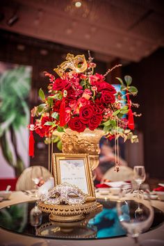 a table topped with a vase filled with red flowers next to a plate and wine glasses