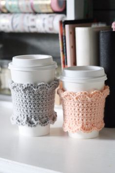 two coffee cups sitting next to each other on a white table with books in the background