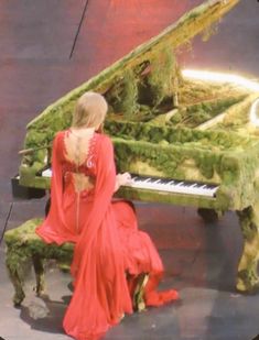 a woman in a red dress sitting at a green piano with moss growing on it