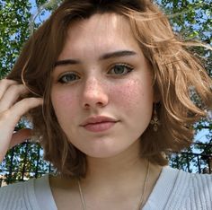 a young woman with freckles on her face and necklace in front of trees