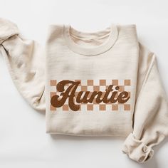 Checkered Auntie Sweatshirt, Retro Auntie Sweater, Gift for Aunt, New Auntie Sweatshirt, Baby Announcement for Aunt, Cool Aunt Sweatshirt  ♥ WHY YOU WILL LOVE YOUR SWEATSHIRT ♥ * Unique cute gift for everyone that is incredibly easy and stress-free to order & receive * Design is a the words Golden mama writing with trendy retro color and font. * Softest quality 50% cotton, 50% polyester with loose fit that runs true to size (unisex) * Extreme comfort with no bulky side seams for great shape and Retro Crew Neck Tops With Name Print, Retro Fall Tops With Lettering, Retro Lettering Tops For Fall, Winter Cotton Top With Name Print, Cotton Top With Name Print For Winter, Fall Sweater With Name Print And Crew Neck, Fall Crew Neck Sweater With Name Print, Auntie Sweater, Auntie Sweatshirt