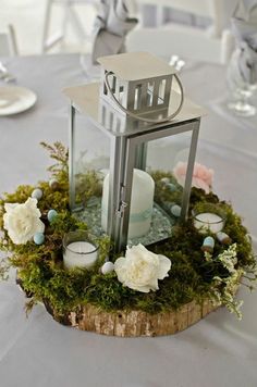 a small lantern with flowers and candles on top of a wooden stump in the center of a table