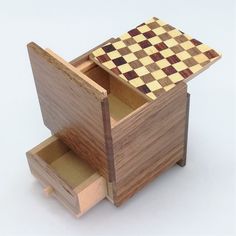 a wooden box with a checkerboard pattern on the lid and drawer opened to show its contents