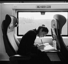 a woman writing on a paper while sitting in a seat next to an open window