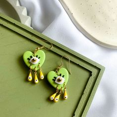 two green birds with yellow beaks are hanging from earwires on a tray