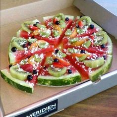 a pizza with many different types of fruits on it in a box, ready to be eaten