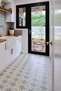 a kitchen with white cabinets and black doors, tiled flooring and open glass door