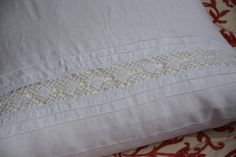 a white pillow on top of a red and white floral print bed spread with an embroidered border