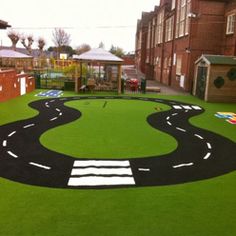 a play area with artificial grass and painted markings on the ground in front of brick buildings