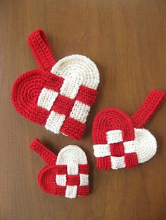 three crocheted heart shaped dishes on a wooden table next to a pair of red and white oven mitts