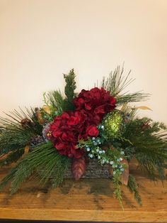 a wooden table topped with a vase filled with red flowers and greenery next to a wall