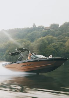 a man driving a speed boat in the water with trees in the backgroud