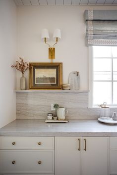 a white kitchen with marble counter tops and gold trim on the window sill above