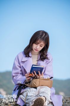 a woman sitting on top of a rock holding a book