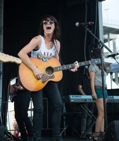 a woman singing into a microphone while holding a guitar