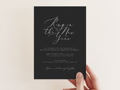 a hand holding up a black and white wedding card with the words, ring in the new year on it