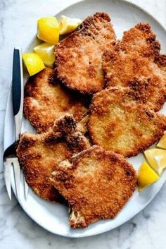 some fried food on a white plate with lemon wedges and a fork next to it