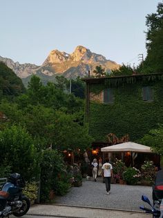 two people are walking towards a house with mountains in the background