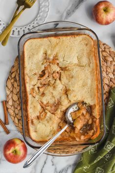 a casserole dish with meat and vegetables in it on a table next to an apple