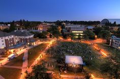 an aerial view of a city at night with people sitting in the grass and lights on