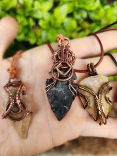 a person's hand holding four different pendants in their palm, with plants behind them