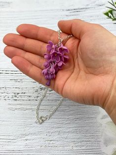 a hand holding a tiny purple flower on a chain