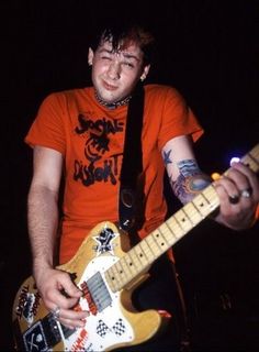 a young man with tattoos playing an electric guitar at a music concert in the dark