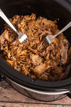 a slow cooker filled with shredded meat and two tongs sticking out of it