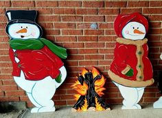 three snowmen standing in front of a brick wall next to a campfire and fire