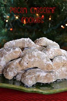 a pile of powdered sugar cookies sitting on top of a green plate next to a christmas tree