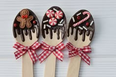 three wooden spoons decorated with chocolate covered cookies and candy canes are on a white surface