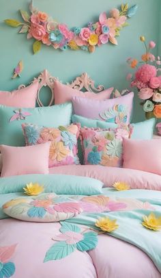 a bed covered in pink and blue comforters with flowers on the wall behind it