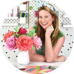 a woman sitting at a table with flowers in a vase and pens on the desk