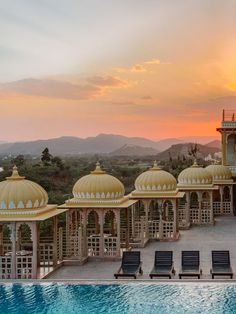 an outdoor swimming pool with several pavilions and lounge chairs in front of it at sunset