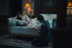 two women sitting on a bed in a dark room, one is touching the foot of another woman