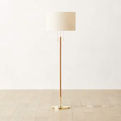 a floor lamp with a white shade on it's side and a gold base