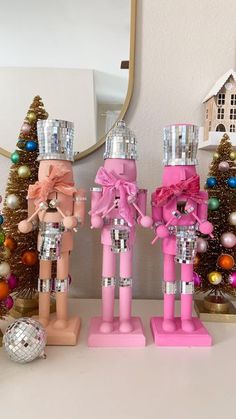 three wooden nutcrackers with pink bows on them are standing in front of a christmas tree