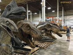 three large dinosaur heads are on pallets in a warehouse with people looking at them