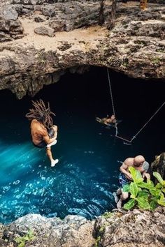 two people jumping into the water from a suspended rope in an underground cave, while another person is on a swing