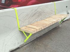 a bench made out of concrete and wood sitting in front of a red car on the street