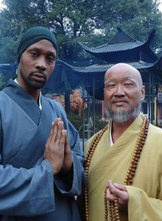 two men standing next to each other with beads around their necks and hands in front of them