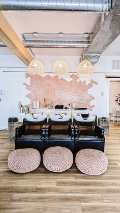 a room with two black couches and three round stools in front of a pink wall