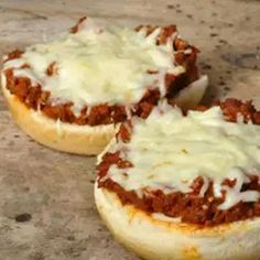 two sloppy joes sitting on top of a wooden table covered in cheese and sauce