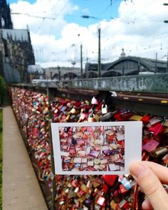 a person holding up a card with many padlocks attached to the fence behind them