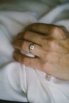 a woman's hand with a diamond ring on top of her finger, resting on a white blanket